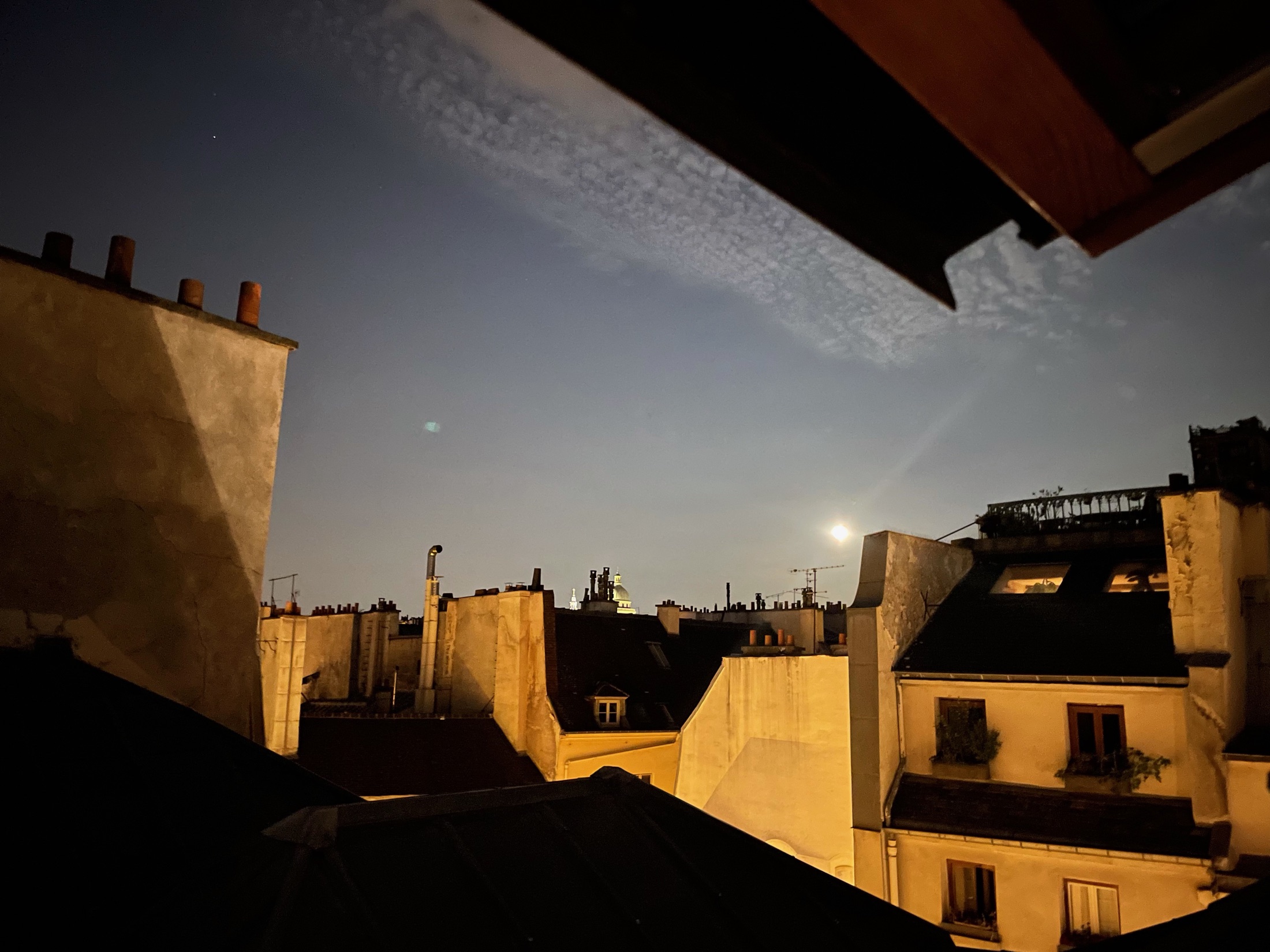 Paris rooftops at dusk from a skylight, moon rising over the Panthéon